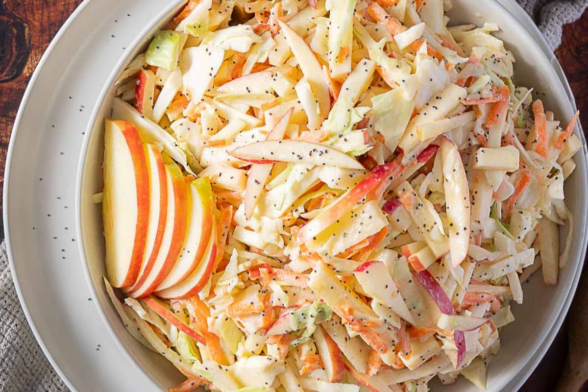 A bowl of coleslaw with shredded cabbage, carrots, and thin apple slices, garnished with poppy seeds-one of the best side dishes and sure to be a show-stealing side at any meal.