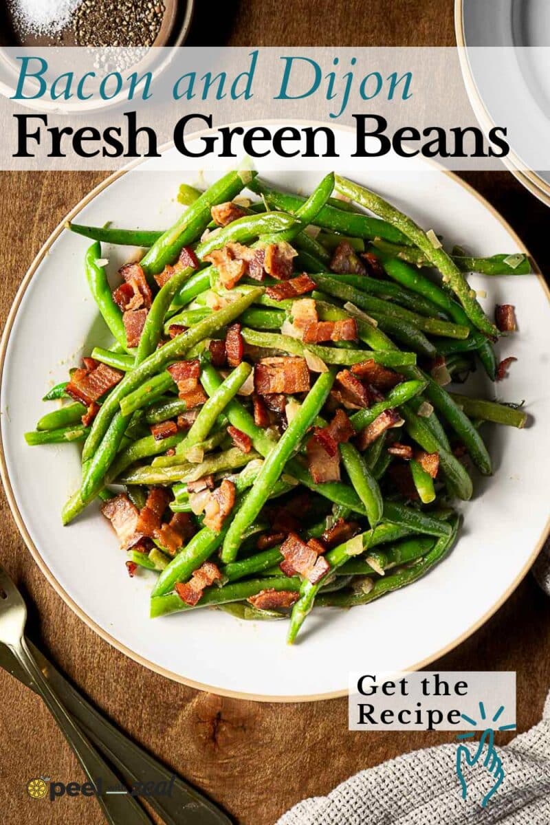 A plate of bacon green beans topped with chopped bacon pieces and sliced onions, placed on a wooden table with a fork and napkin nearby.