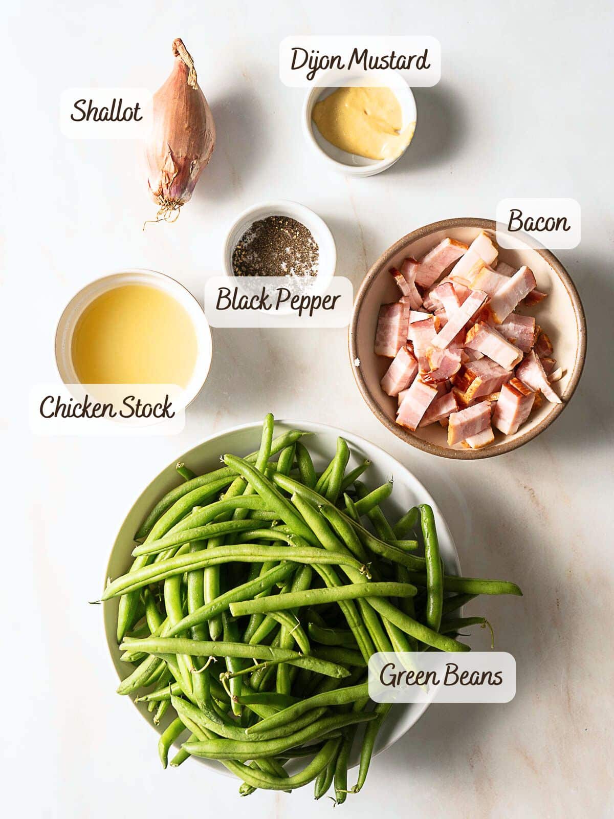 Ingredients for bacon green beans laid out on a white surface: fresh green beans, diced bacon, shallot, chicken stock, Dijon mustard, and black pepper.