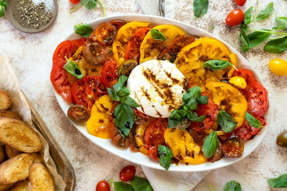 A platter of sliced heirloom tomatoes with fresh basil, burrata cheese, and balsamic glaze makes one of the best easy side dishes for dinner sides or weeknight sides, served with toasted bread on the side.