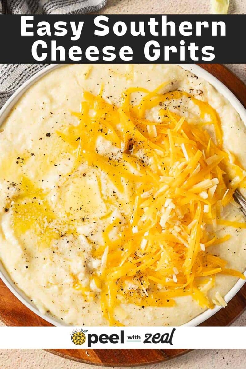 A bowl of creamy cheddar grits topped with shredded cheddar cheese and black pepper, served with a spoon on the side.