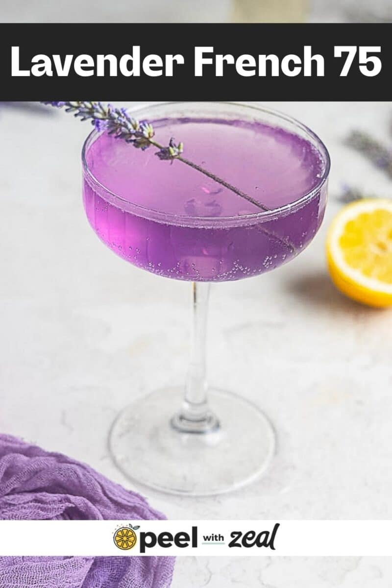 A coupe glass filled with a vibrant lavender French 75 cocktail, garnished with a sprig of lavender, sits beside a half lemon and purple cloth. Text reads "Lavender French 75.