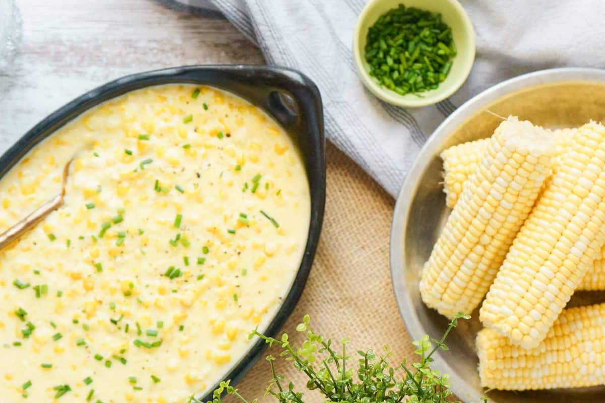 A dish of creamy corn topped with chopped chives sits next to a bowl of corn on the cob and a small bowl of more chives-a perfect addition to your collection of soul-warming recipes.