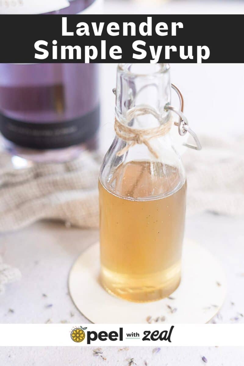 A small glass bottle filled with light brown lavender simple syrup sits on a white coaster, with a purple bottle and soft fabric in the background.