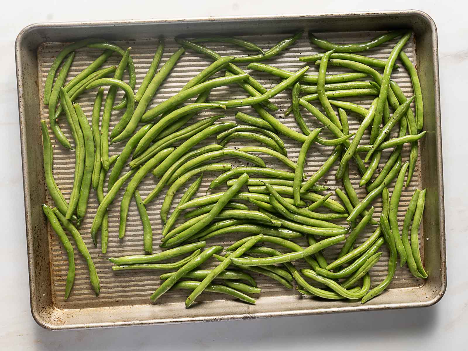 A baking sheet filled with raw green beans spread out evenly, ready for roasting.