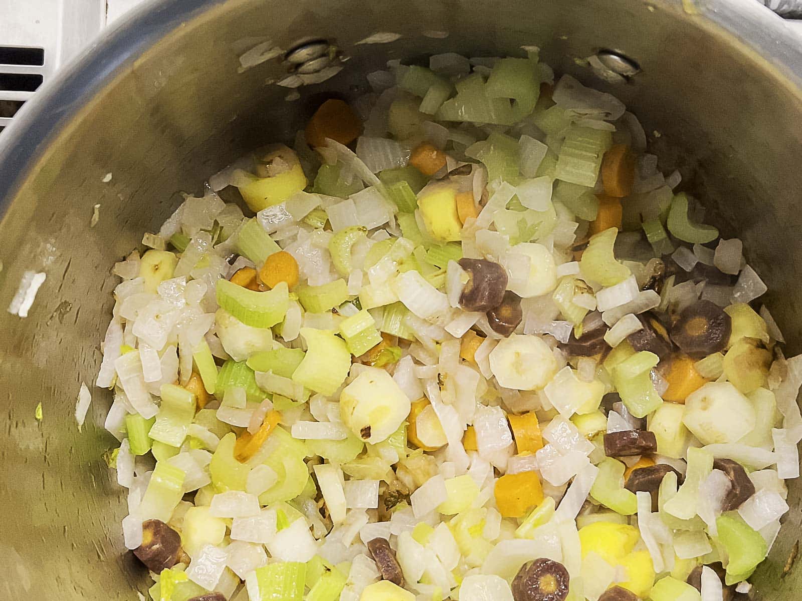 Chopped onions, celery, and multicolored carrots are being saut&eacute;ed in a stainless steel pot.
