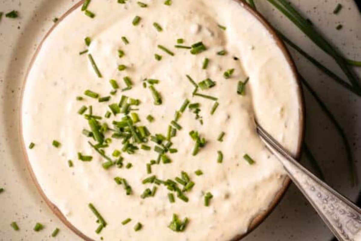 A bowl of creamy white dip topped with chopped chives, with a spoon resting inside-perfect as a next-level steak sauce to elevate your favorite cuts.