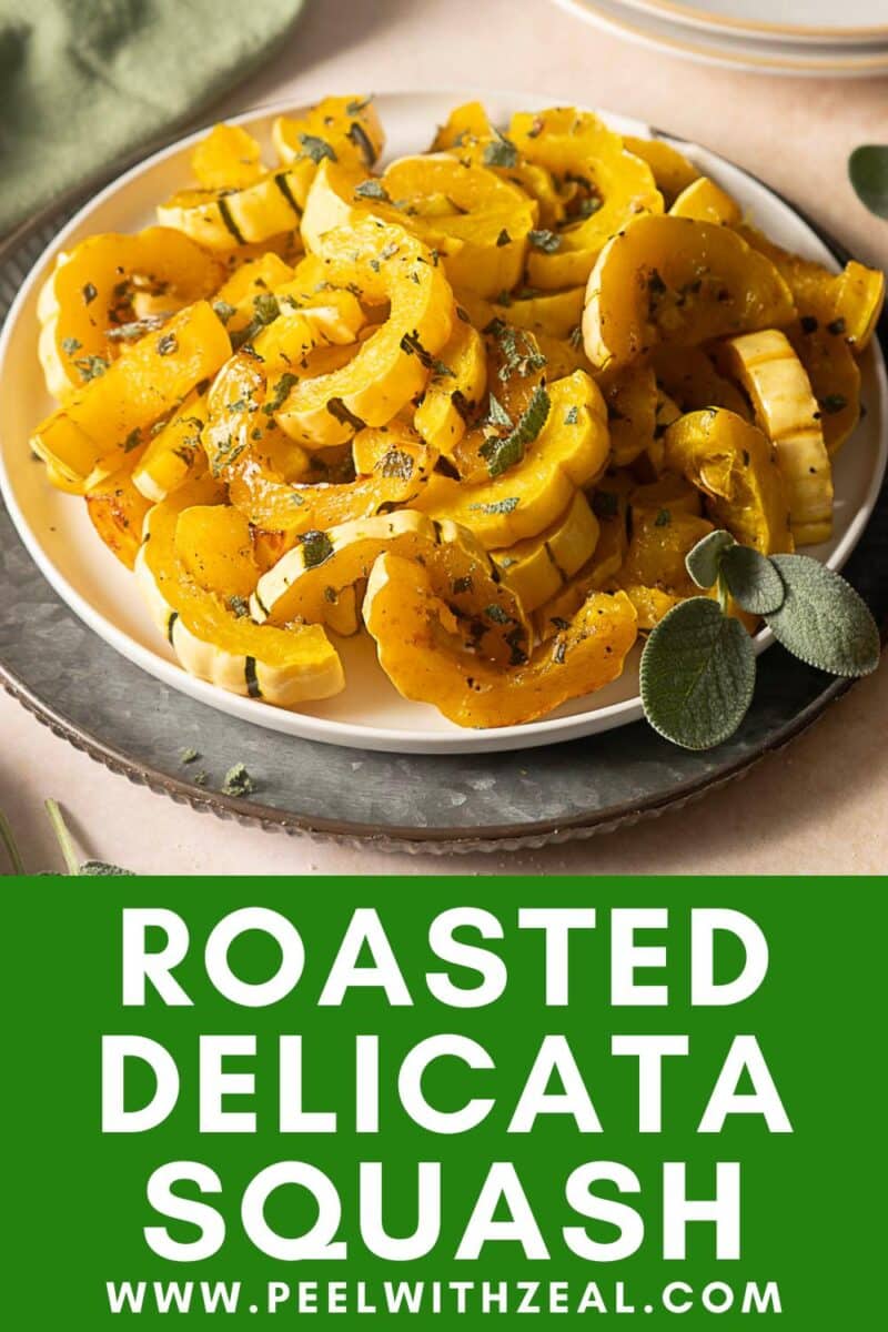 A plate of Roasted Delicata Squash slices garnished with herbs sits on a gray dish, with fresh sage next to the plate.