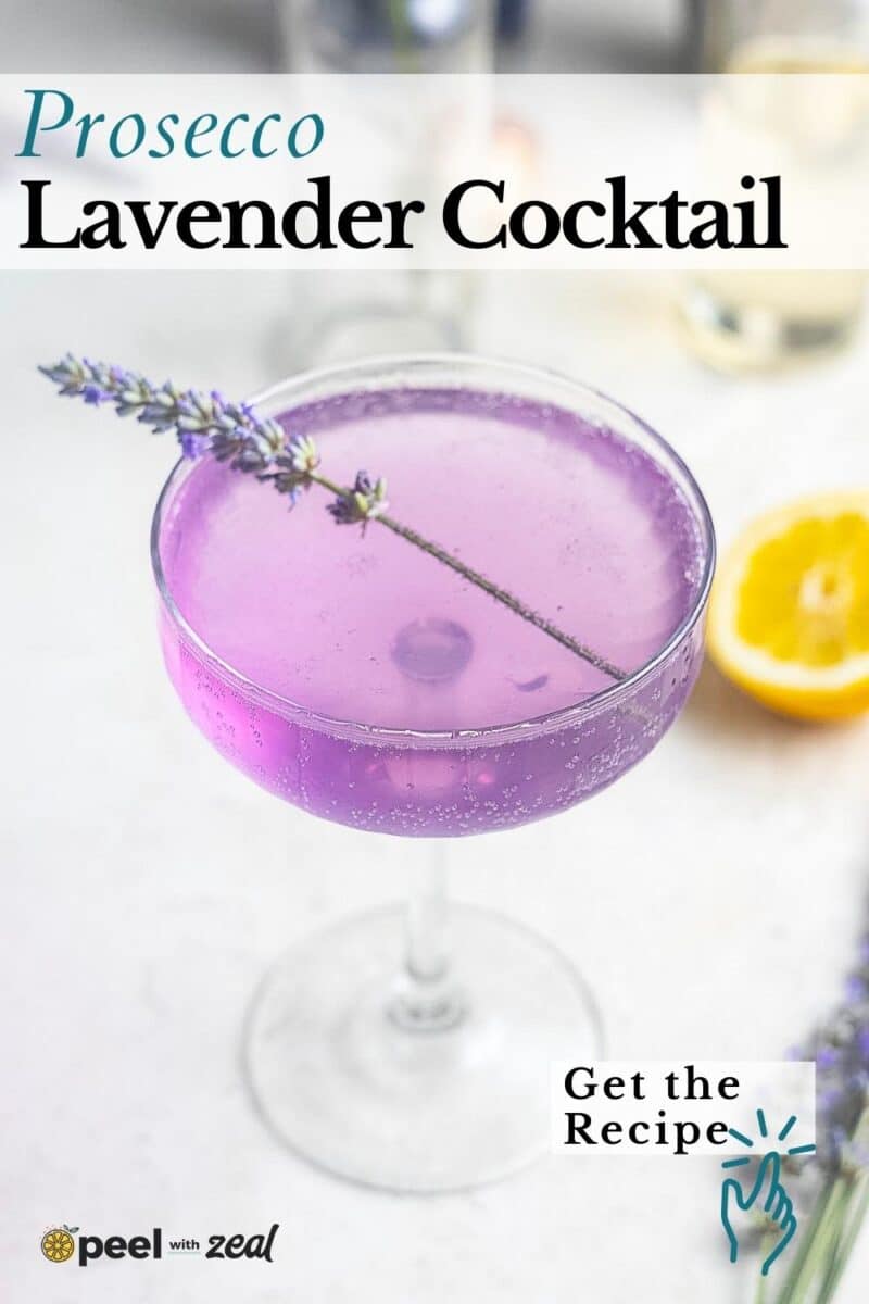 A coupe glass with a purple Lavender French 75 cocktail, garnished with a lavender sprig, set on a light surface with a lemon half in the background.