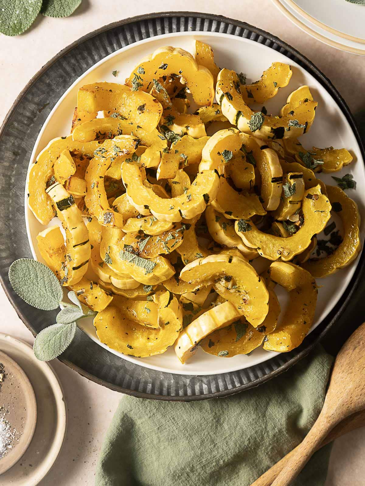 A plate of roasted delicata squash slices garnished with fresh herbs, served on a round white dish with a black rim.