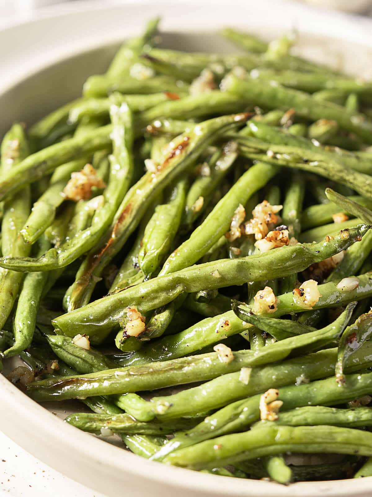 A plate of cooked green beans garnished with chopped garlic and seasoning.