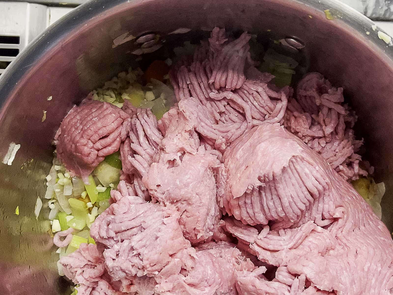 Ground turkey is added to a pot containing chopped onions, celery, and other vegetables, ready to be cooked.