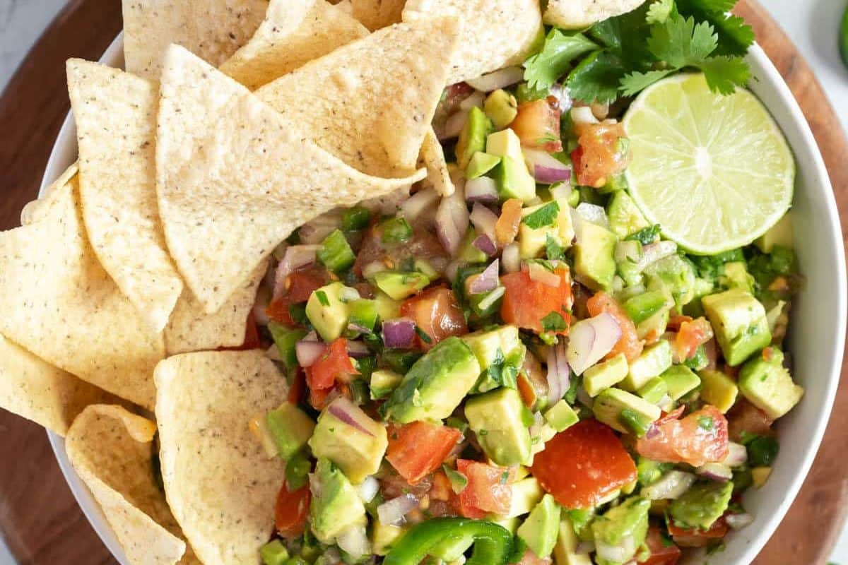 A bowl of avocado salsa with diced tomatoes, onions, jalape&ntilde;os, and cilantro-one of the ultimate Game Day Dips-served with tortilla chips and a lime wedge for a touchdown snack.