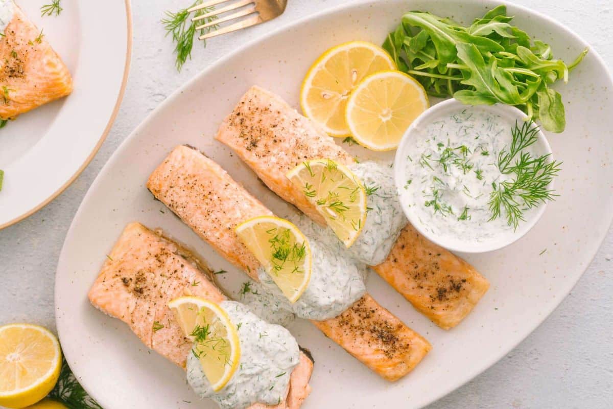 Three baked salmon fillets topped with creamy dill sauce, garnished with lemon slices and fresh dill, served with arugula-perfect for quick family recipes and ready in just 30 minutes.