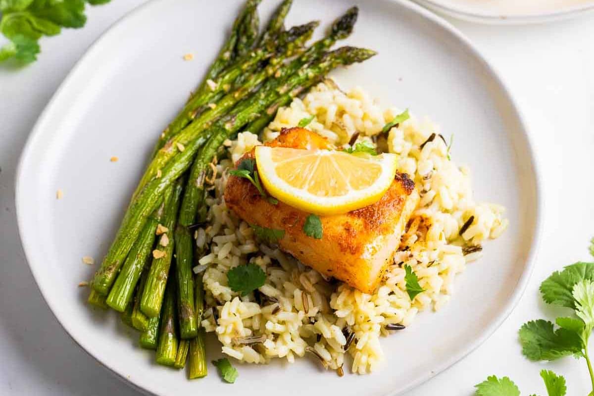Grilled asparagus, seasoned rice, and a piece of fish topped with lemon slices are arranged on a white plate-perfect for quick family recipes or easy 30 minute meals.