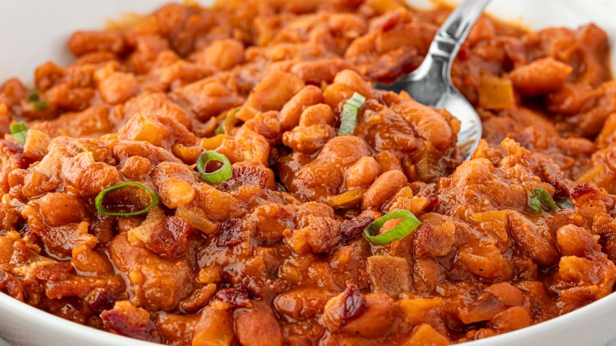 A close-up of baked beans in a bowl, garnished with chopped green onions, with a spoon partially visible—perfect for pairing alongside your favorite seasonal apple dishes or apple desserts.