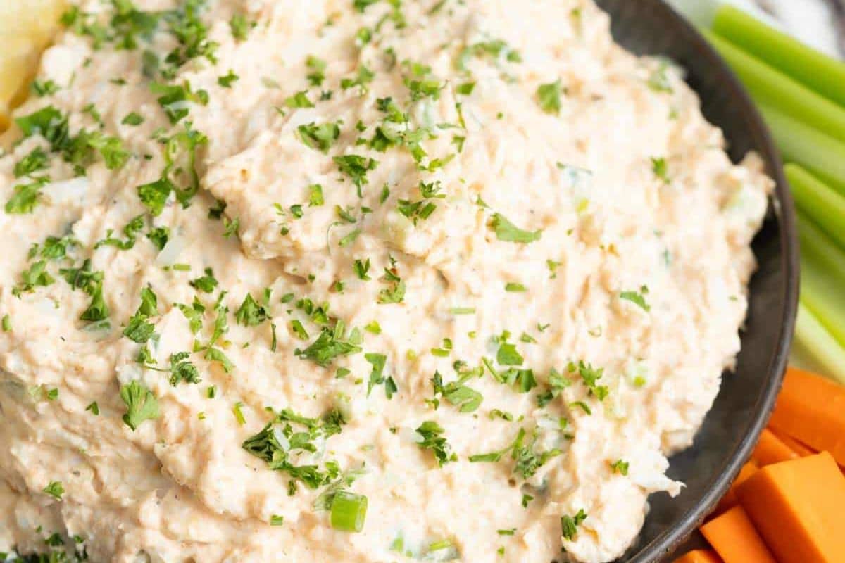 A close-up of a creamy Game Day Dip garnished with chopped parsley, served in a dark bowl with celery and carrot sticks on the side-perfect for scoring a touchdown at your next gathering.