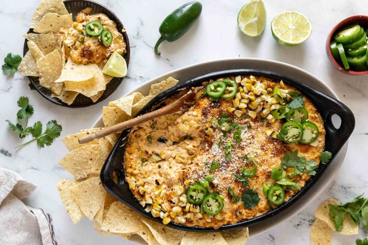 Oval dish of cheesy corn dip topped with jalape&ntilde;o slices and cilantro, surrounded by tortilla chips-perfect for Game Day Dips. Limes and extra jalape&ntilde;o slices on the side make this a true touchdown for snack lovers.