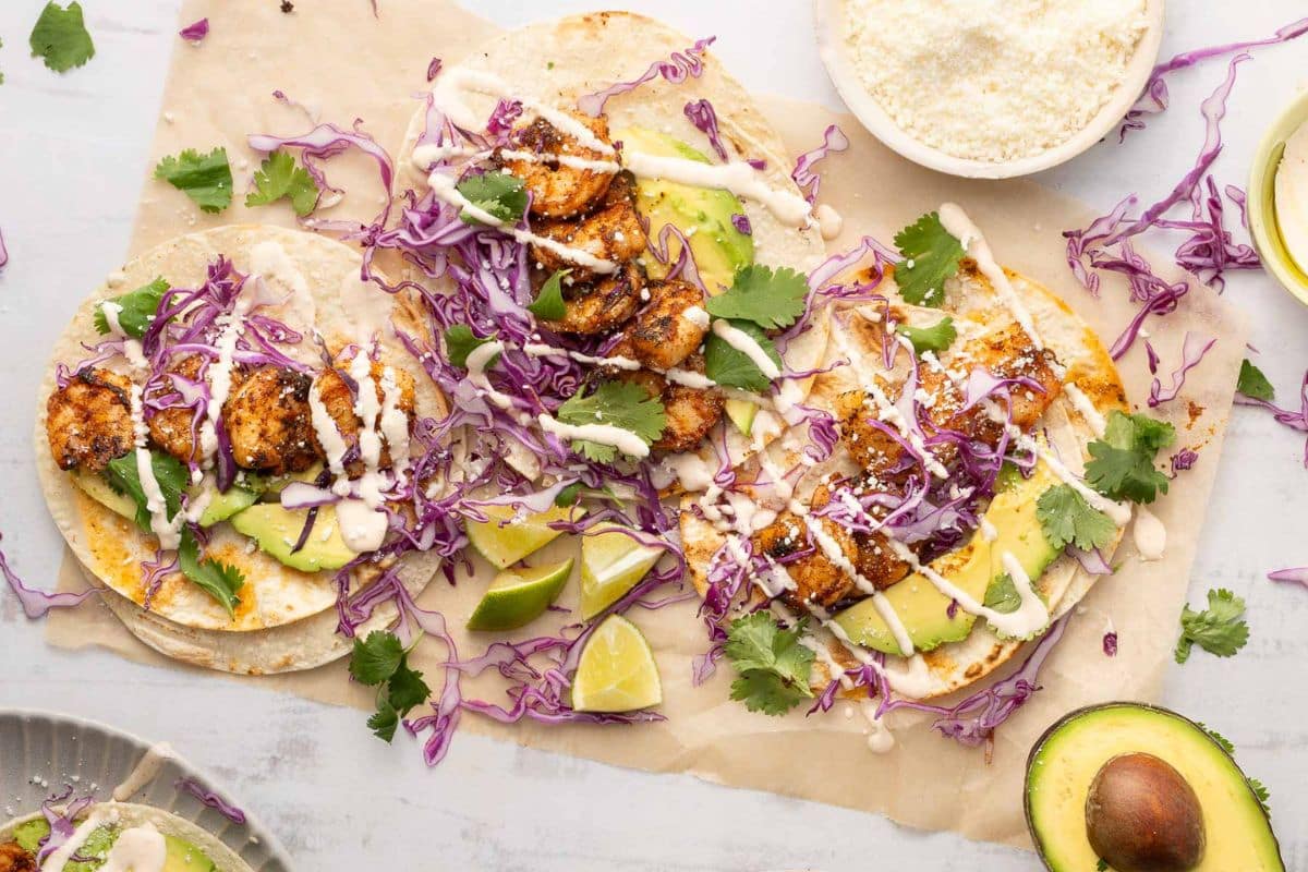 These shrimp tacos with avocado, red cabbage, cilantro, and white sauce make perfect 30 Minute Meals. Served on tortillas and garnished with lime wedges, they're ideal for quick recipes or easy family dinners.
