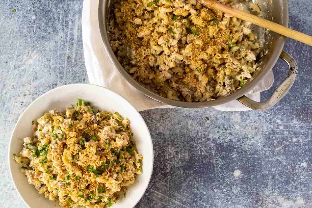 A bowl and a pot of macaroni and cheese topped with breadcrumbs and herbs, with a wooden spoon resting in the pot-perfect for quick recipes or family dinners.
