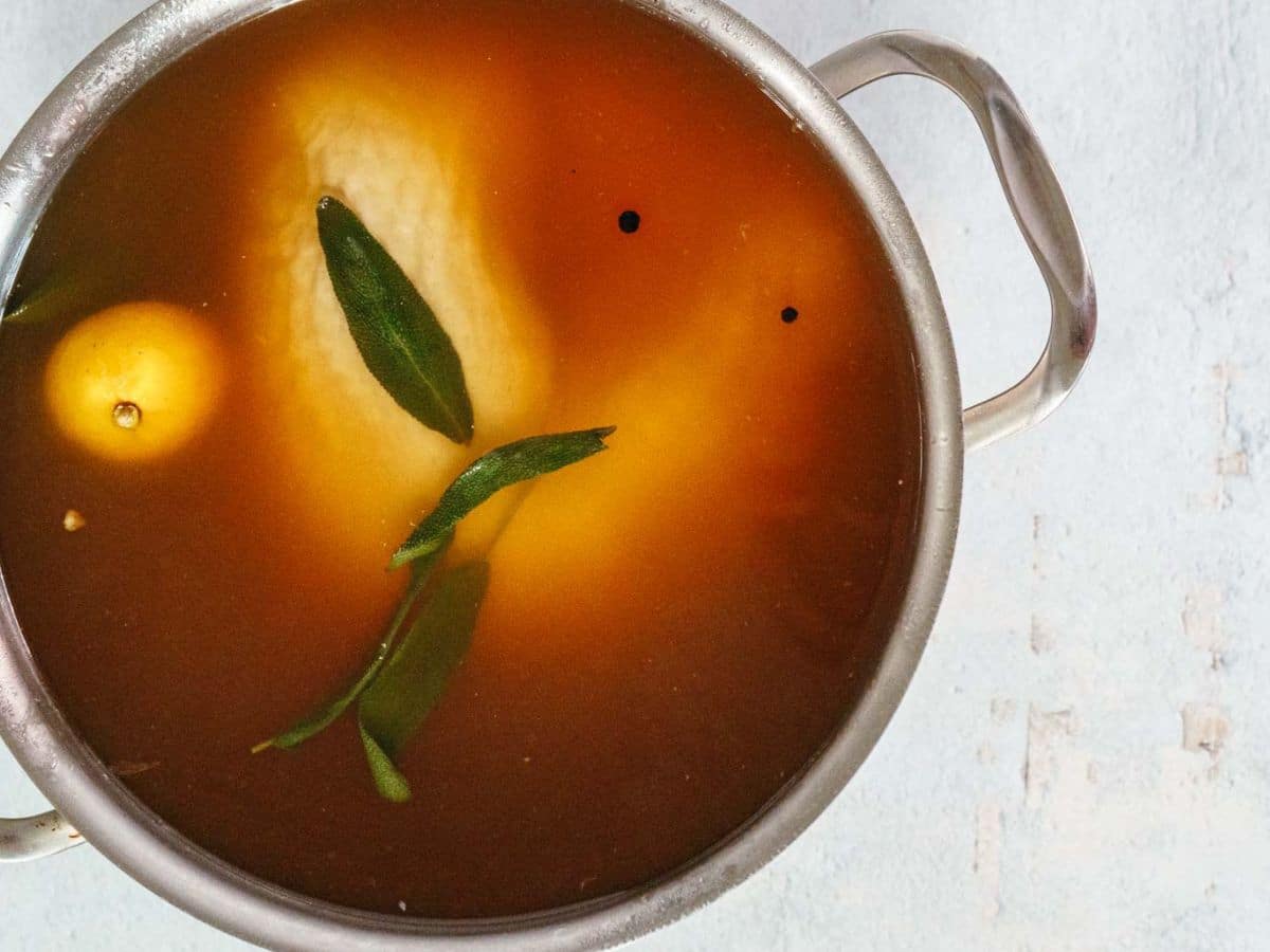 A metal pot filled with salt brine, herbs, a submerged turkey breast.