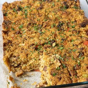 A baked casserole with a golden breadcrumb topping, garnished with chopped herbs, in a glass baking dish with one piece removed.