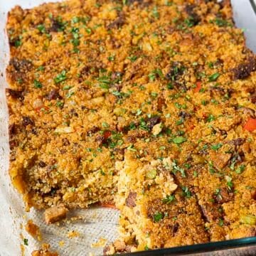 A baked casserole with a golden breadcrumb topping, garnished with chopped herbs, in a glass baking dish with one piece removed.