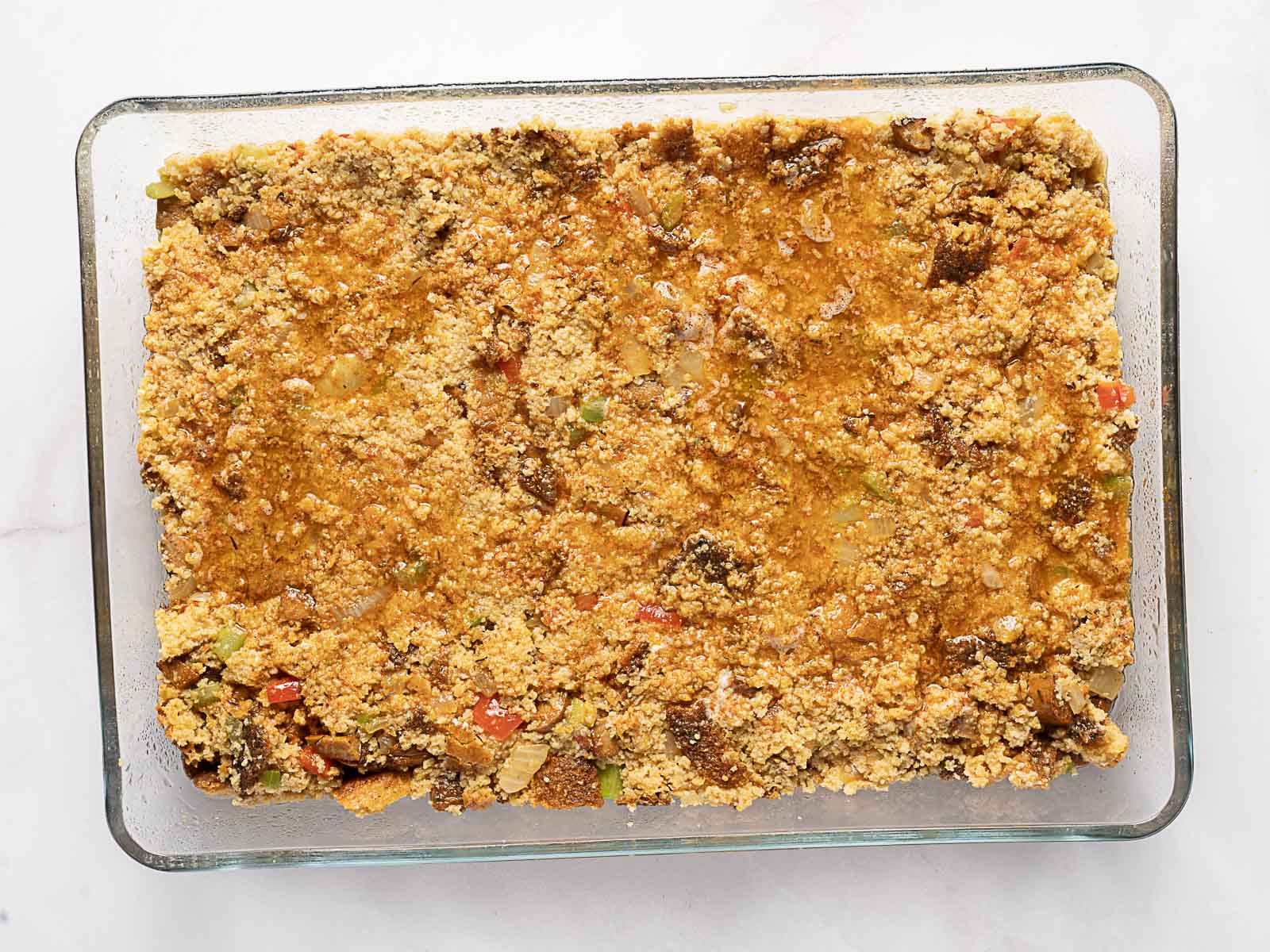 A glass baking dish filled with a baked cornbread dressing or casserole, showing a golden-brown, crumbly top with visible vegetables mixed in.