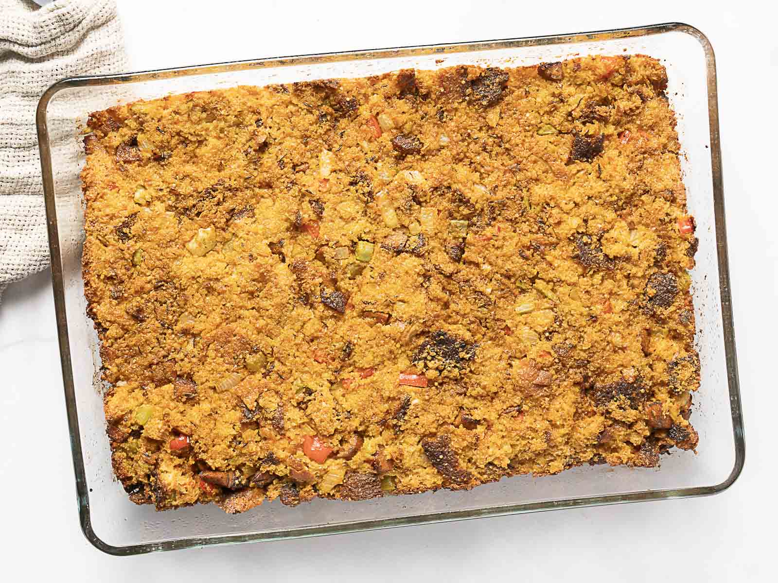 A rectangular glass baking dish filled with golden-brown cornbread stuffing featuring visible pieces of bread and diced vegetables.