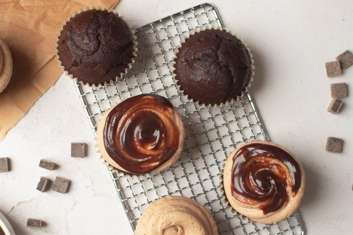 Chocolate cupcakes and cupcakes with swirled chocolate frosting are placed on a wire cooling rack, with chocolate chunks scattered nearby.