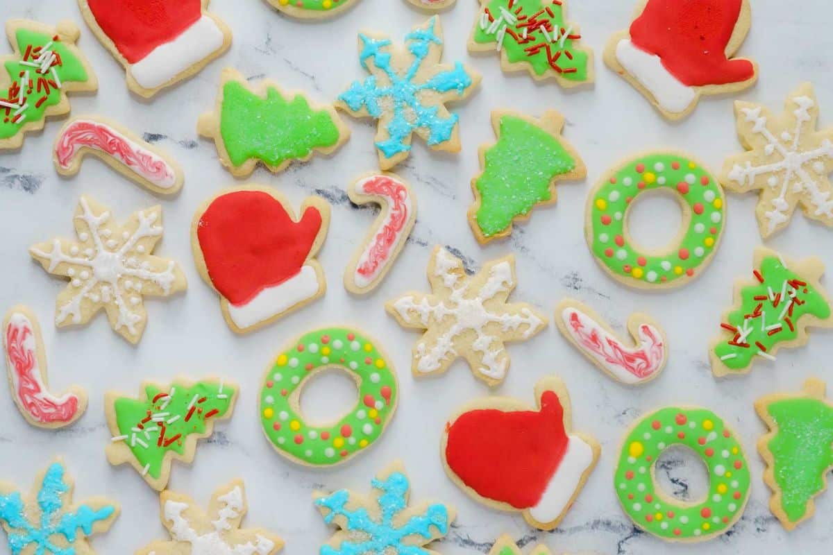 Assorted Christmas-themed sugar cookies decorated with icing, including trees, snowflakes, wreaths, candy canes, and Santa hats, arranged on a white marble surface.