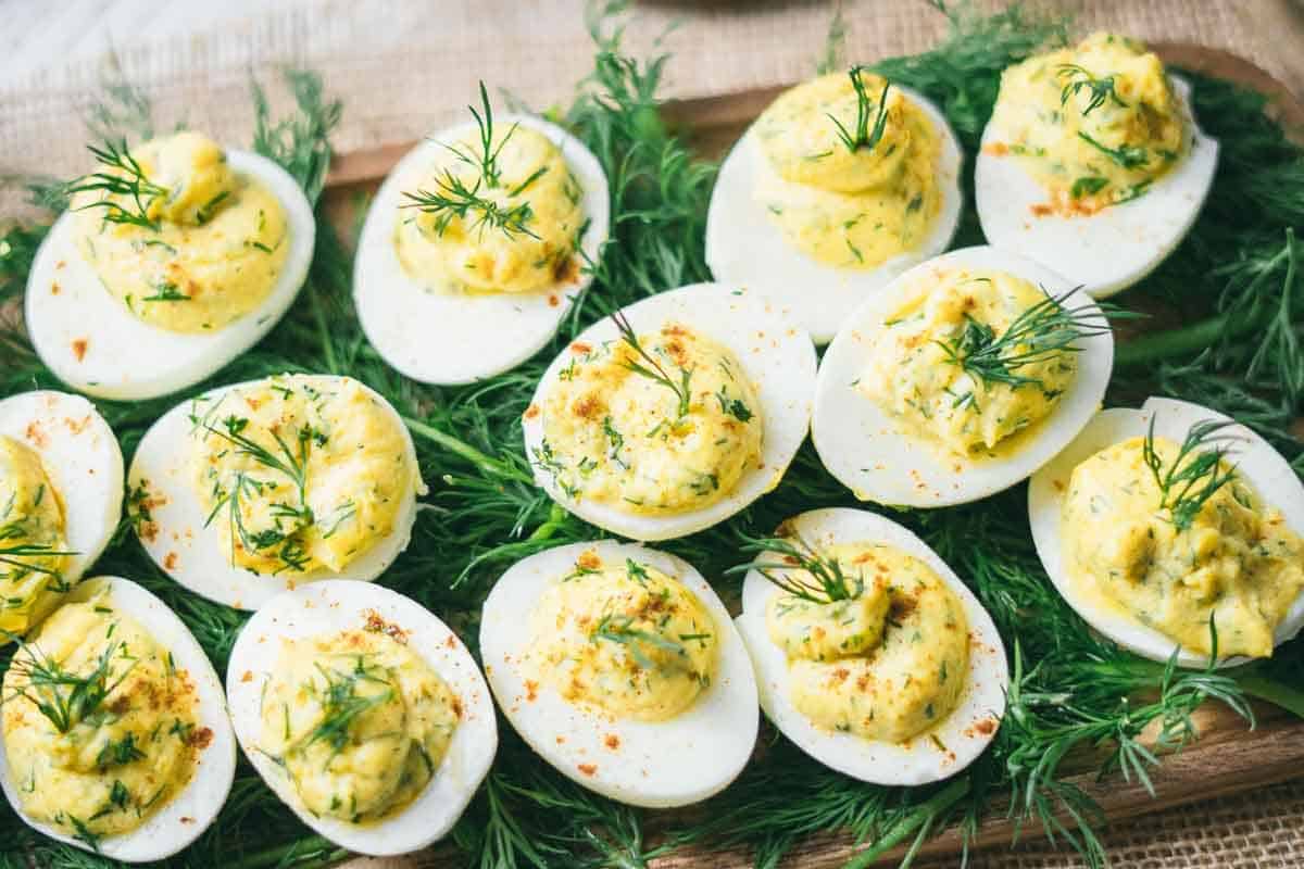A wooden tray filled with deviled eggs garnished with fresh dill and sprinkled with seasoning, perfect for holiday appetizers and festive party gatherings.