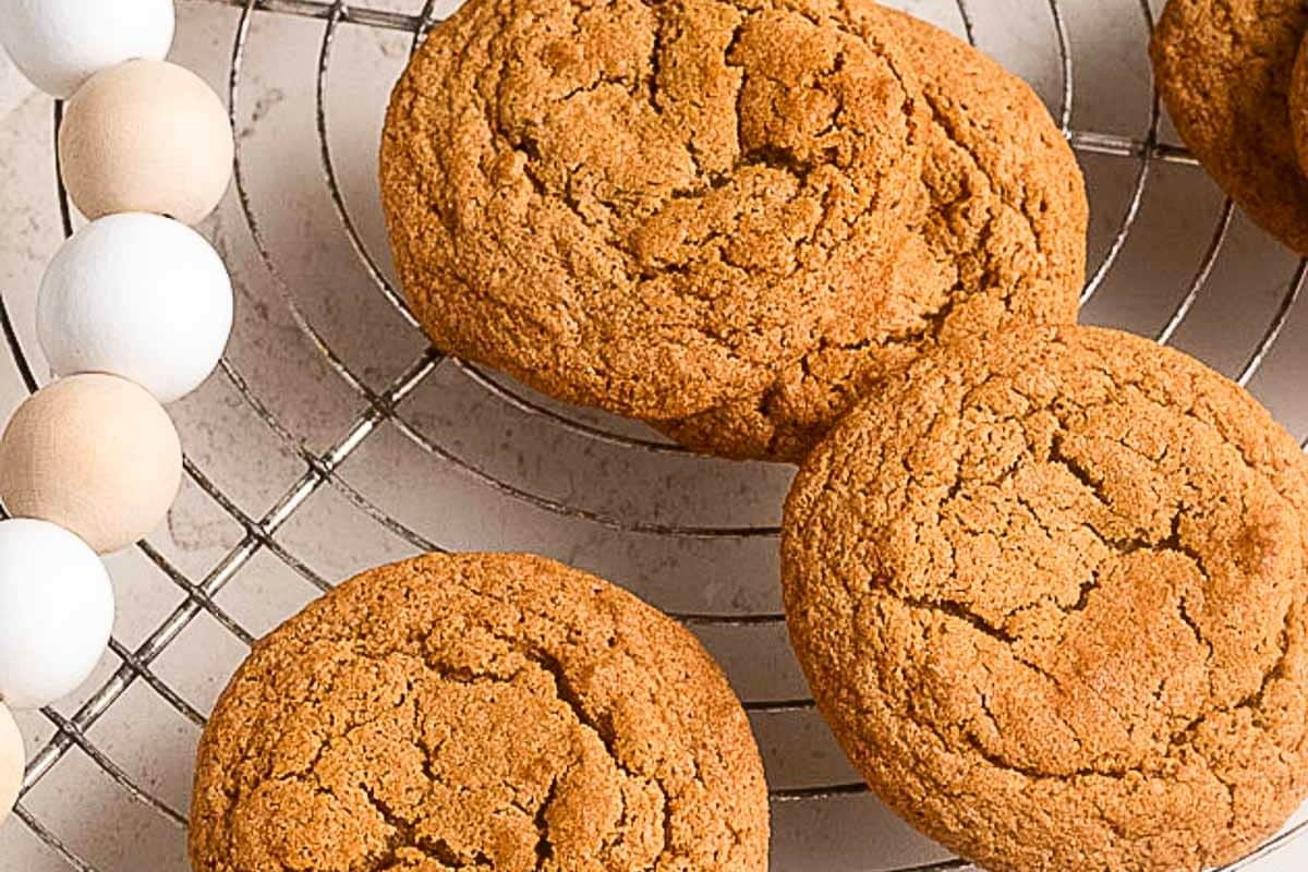 Three golden brown cookies rest on a metal cooling rack, with part of a decorative wooden bead garland visible on the side.