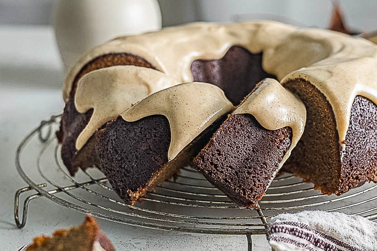 A sliced bundt cake with a light brown glaze sits on a wire cooling rack, with one piece partially removed.