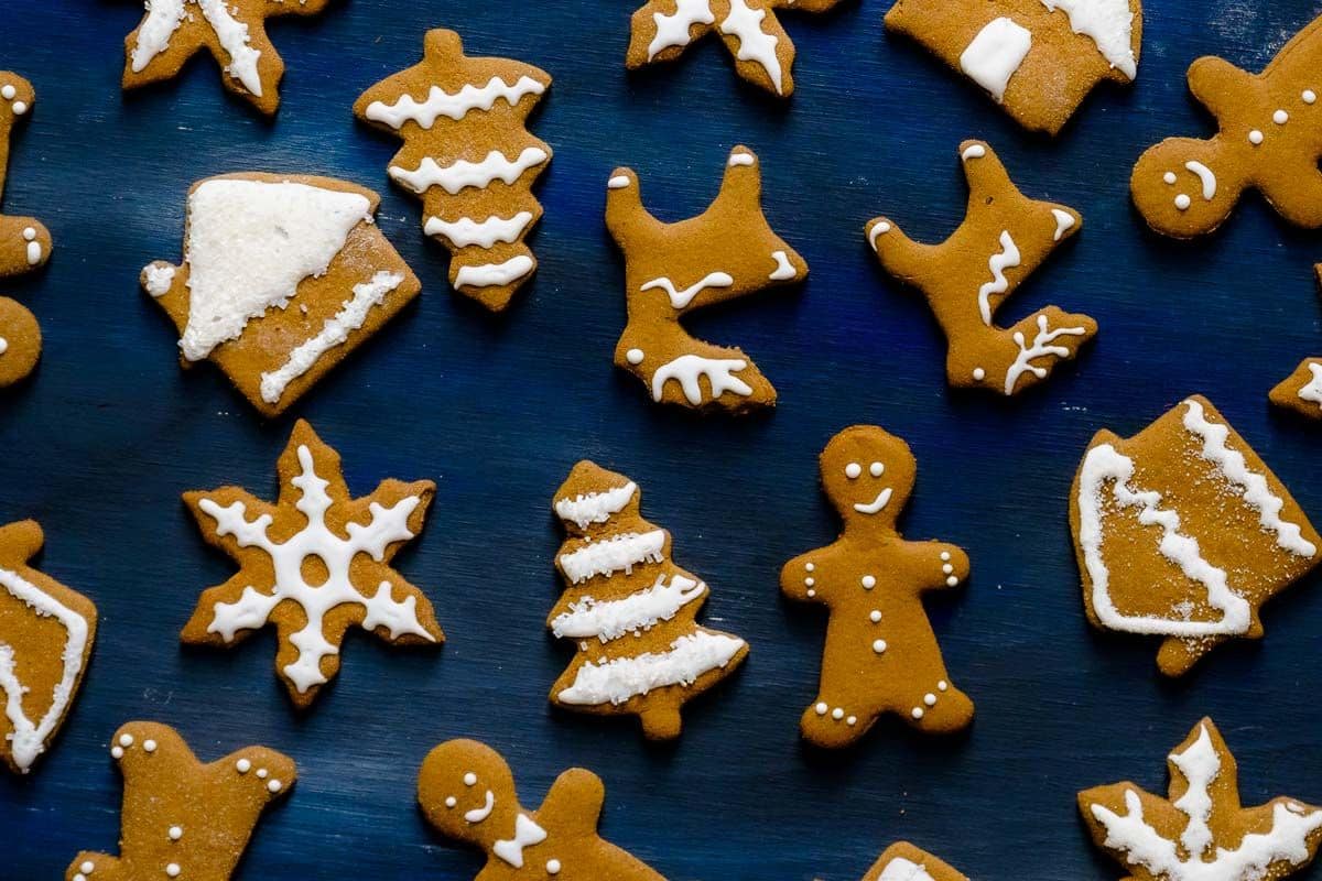 Assorted gingerbread cookies shaped like trees, snowflakes, and people, decorated with white icing, arranged on a dark blue surface.