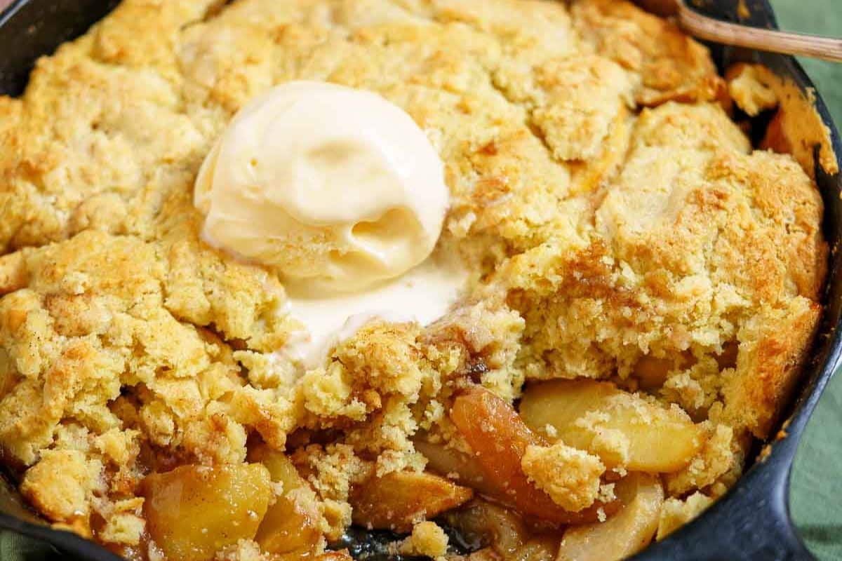 Baked apple cobbler with a golden biscuit topping, served in a cast iron skillet and topped with vanilla ice cream-a cozy favorite among gluten-free Thanksgiving desserts.