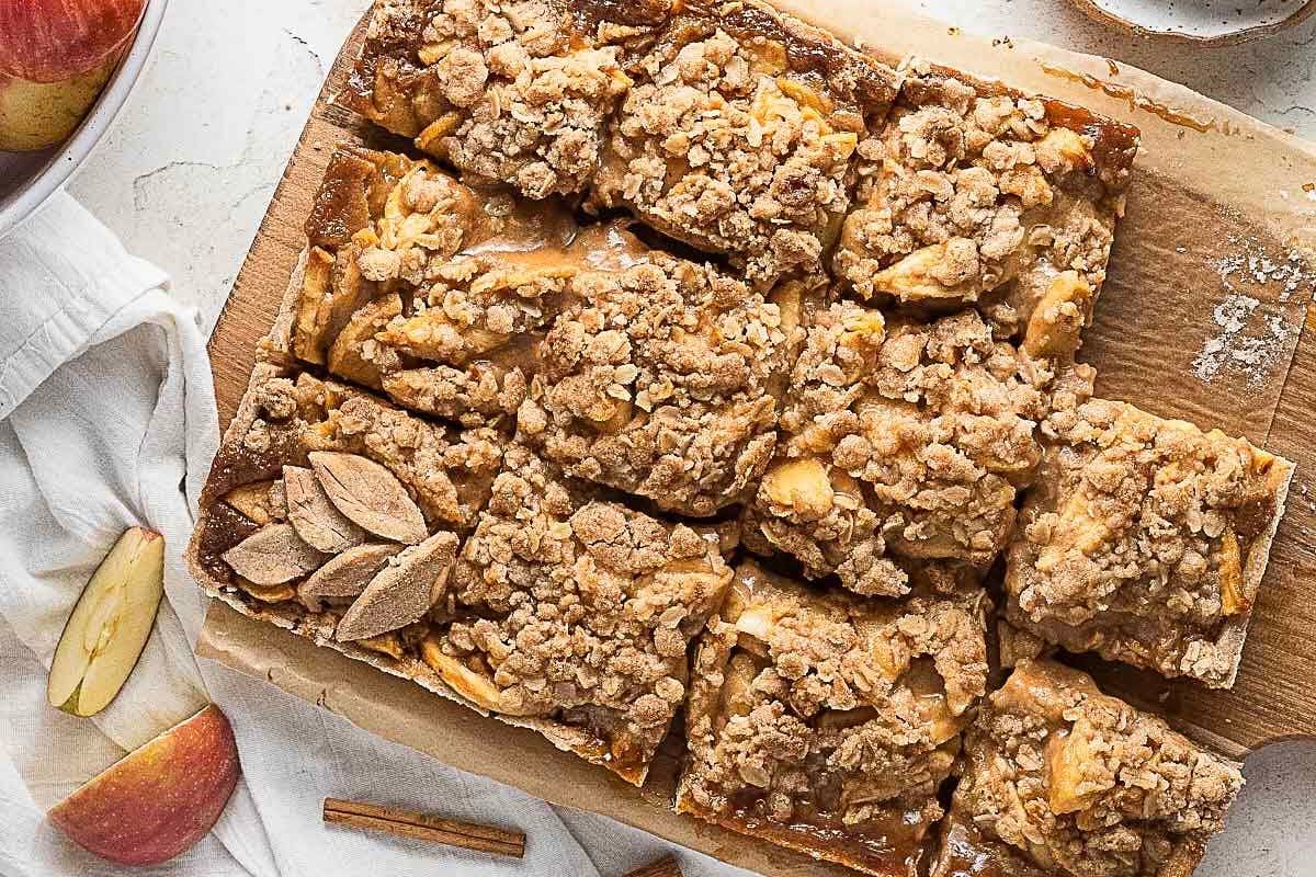 A tray of apple crumble bars cut into squares on a wooden board, with some apple slices and cinnamon sticks nearby-perfect as gluten-free Thanksgiving desserts everyone will love.