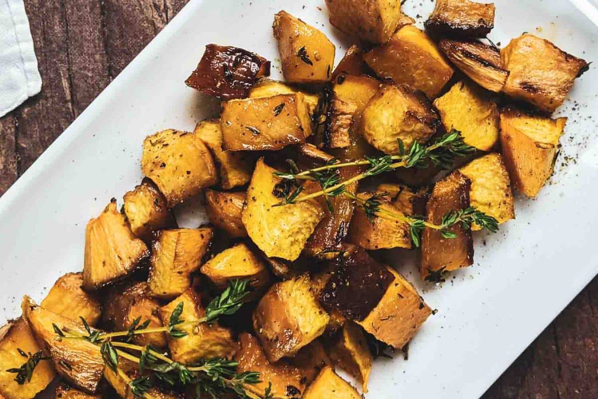 Roasted golden brown root vegetables garnished with sprigs of fresh herbs on a white rectangular plate-perfect as one of your Thanksgiving sides or holiday side dishes.