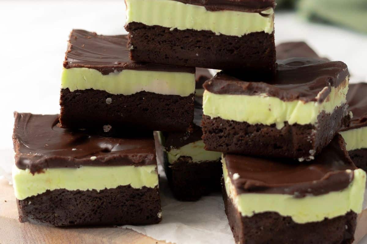 A stack of chocolate mint brownies with a dark chocolate base, a green mint layer in the middle, and a chocolate topping.