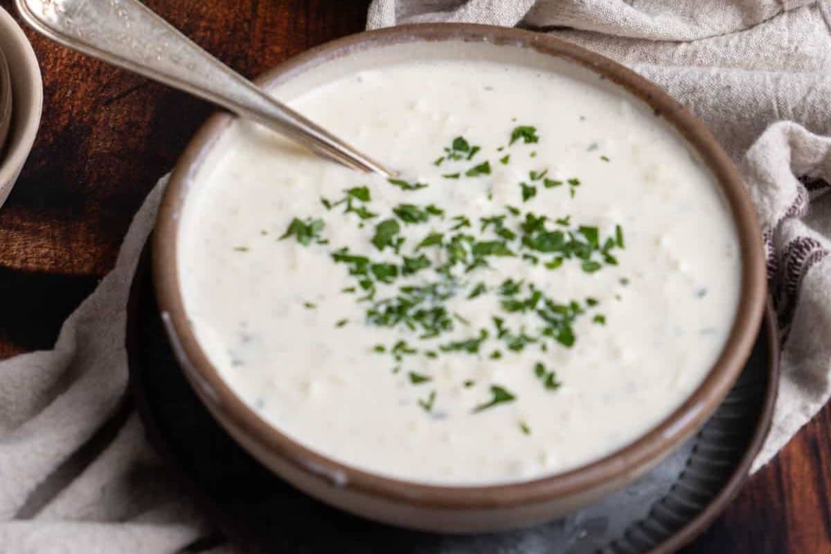 A bowl of creamy white soup garnished with chopped herbs, with a spoon resting inside the bowl-perfect for serving as one of your holiday appetizers.