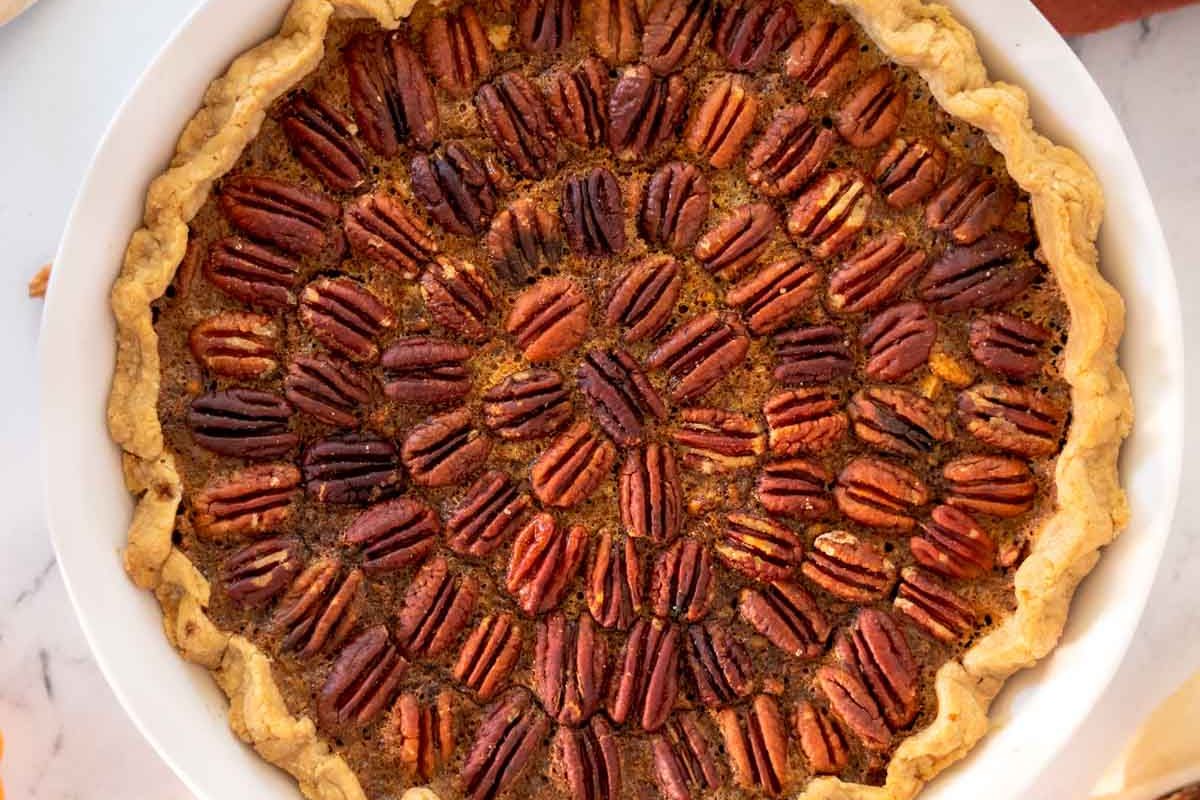 A baked pecan pie with a golden, gluten-free crust, topped with whole pecan halves arranged in a circular, decorative pattern-perfect for Christmas desserts or ending any meal on a sweet note.