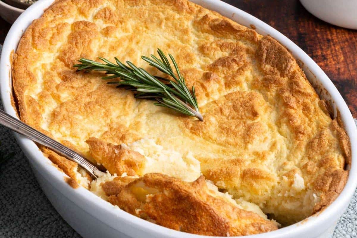 A baked casserole dish with a golden mashed potato topping, perfect for Thanksgiving Sides, garnished with a sprig of rosemary and served with a spoon.