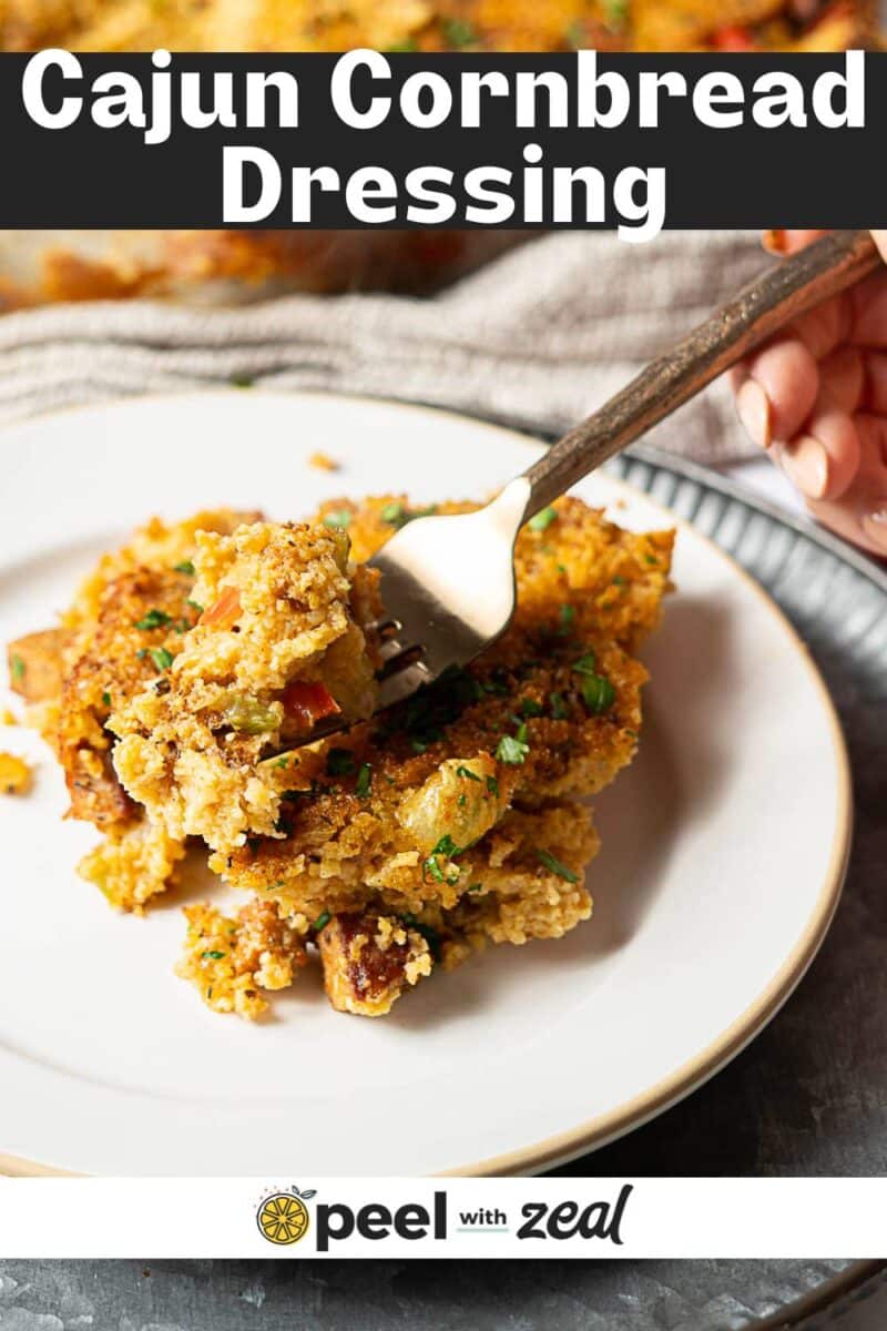 A plate of Cajun Cornbread Dressing topped with chopped herbs, with a fork taking a bite. Text above reads "Cajun Cornbread Dressing," highlighting this flavorful Southern classic.