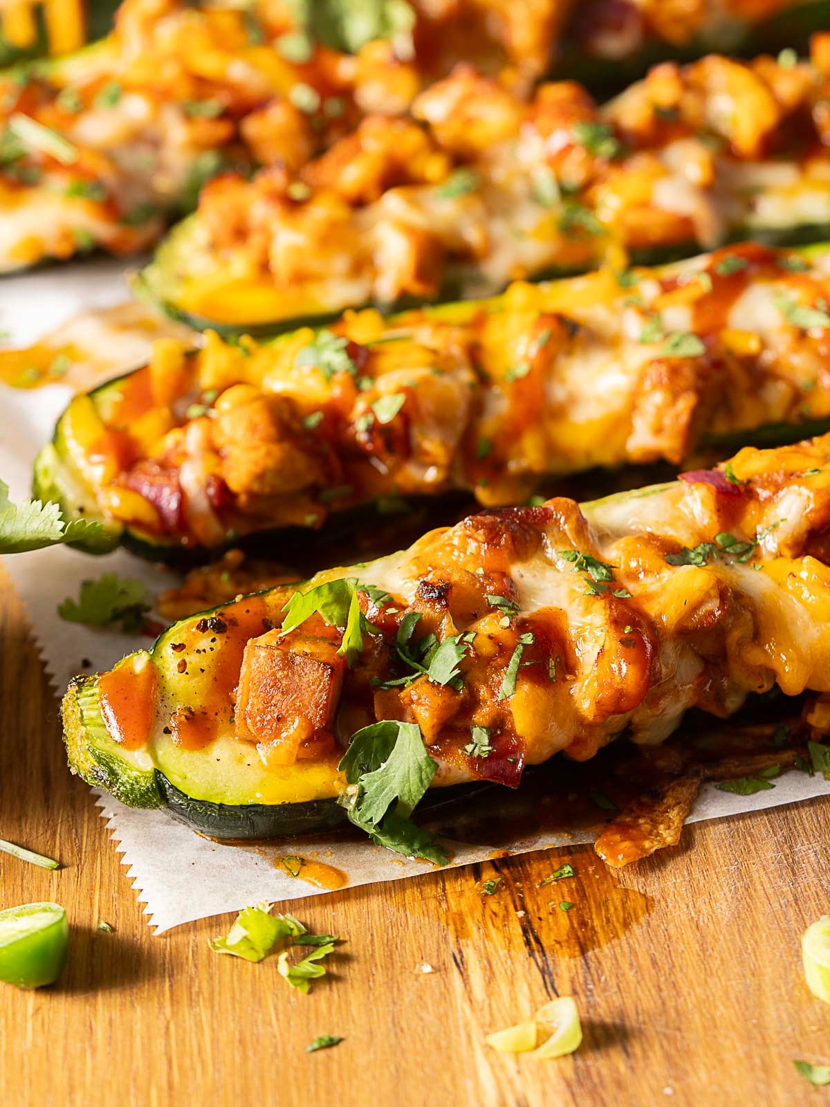 Close-up of zucchini boats stuffed with cheese, chicken, and herbs, placed on parchment paper atop a wooden surface.