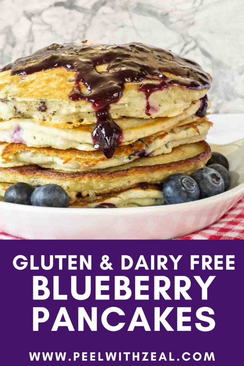 A stack of blueberry pancakes topped with blueberry sauce is on a white plate, with fresh blueberries on the side. A purple banner at the bottom reads “Gluten & Dairy Free Blueberry Pancakes” with a website link.