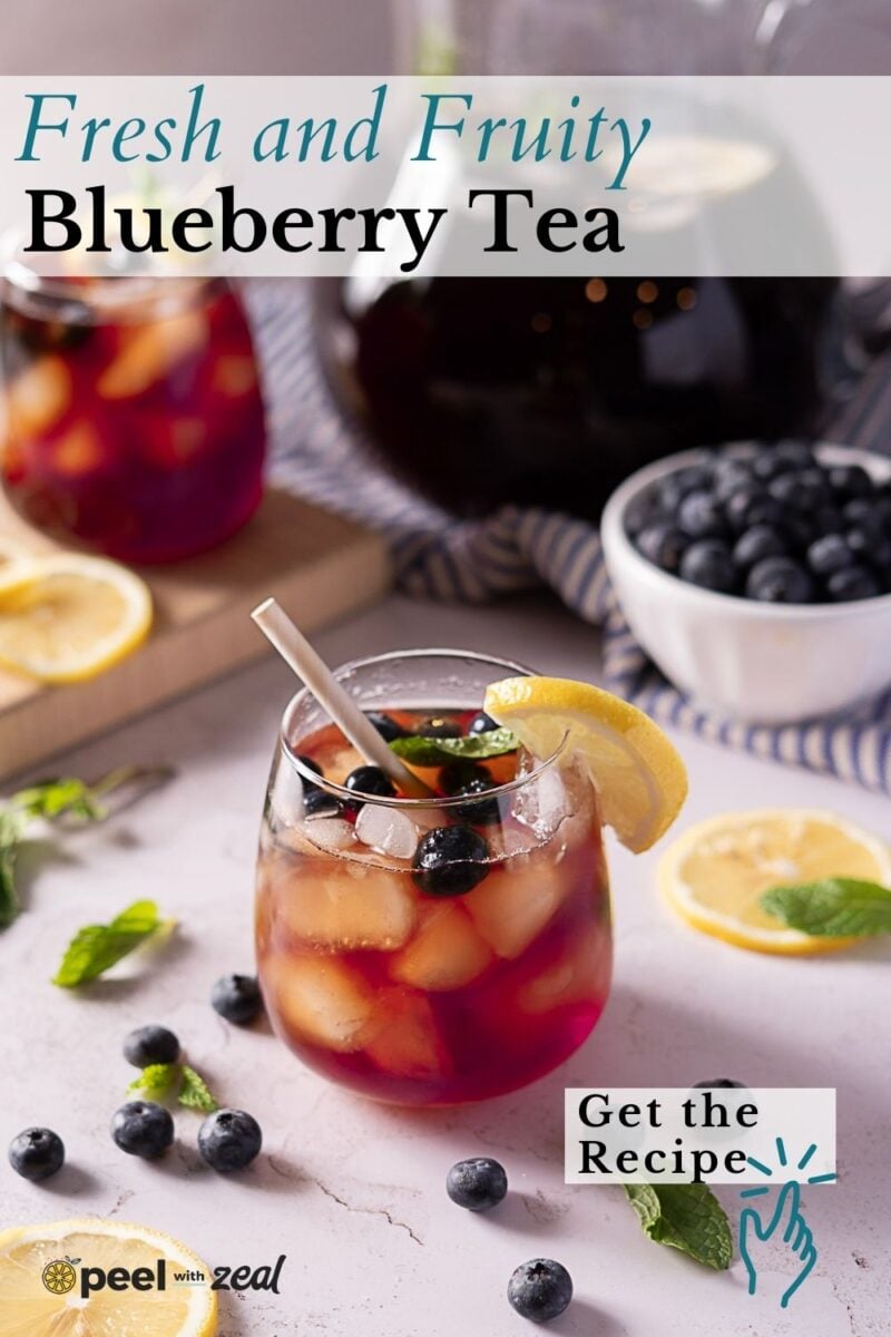 A glass of iced blueberry tea garnished with blueberries, a lemon slice, and mint, sits on a white surface with more blueberries, lemon slices, and a jug of tea in the background. Text reads, “Fresh and Fruity Blueberry Tea.”.