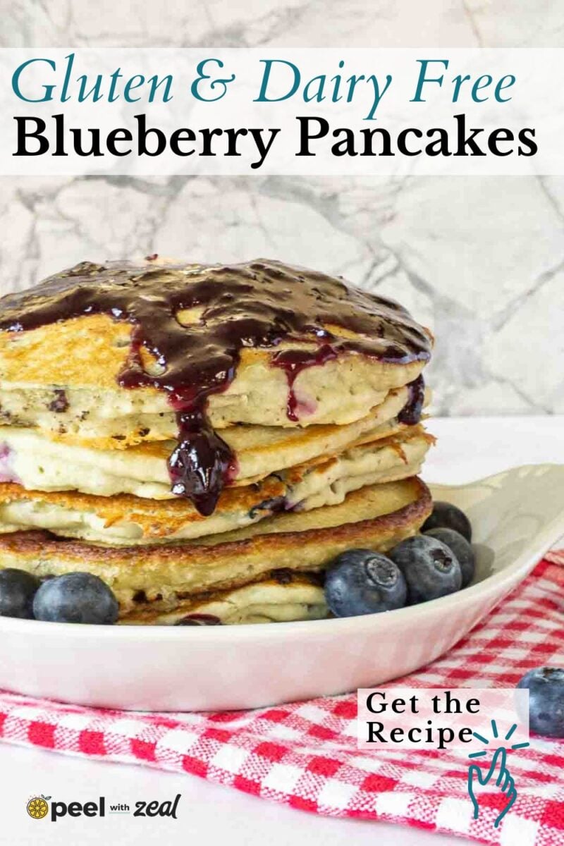 A stack of pancakes topped with blueberry sauce sits on a white plate with fresh blueberries, placed on a red checkered cloth. The text reads “Gluten & Dairy Free Blueberry Pancakes. Get the Recipe.”.