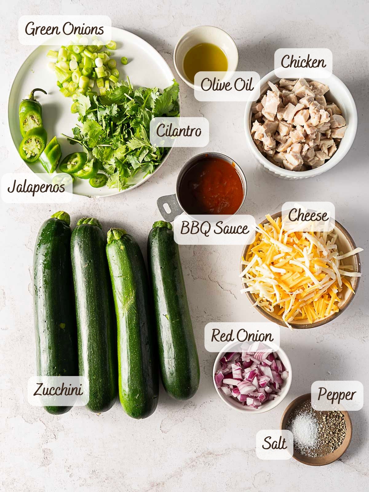 A top view of labeled ingredients including green onions, cilantro, jalapenos, zucchini, olive oil, BBQ sauce, chicken, cheese, red onion, salt, and pepper.