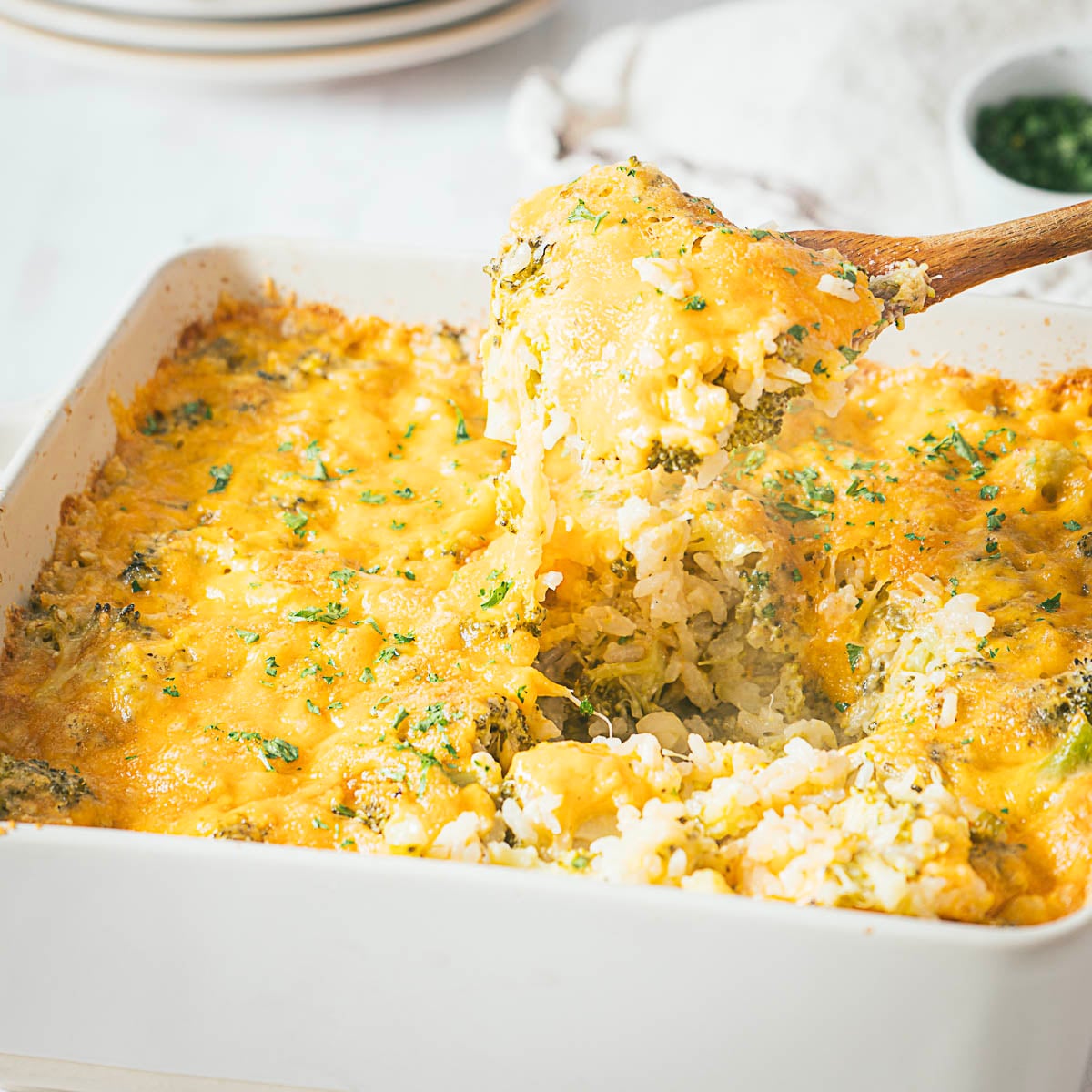 A casserole dish with cheese, broccoli and rice being scoop.