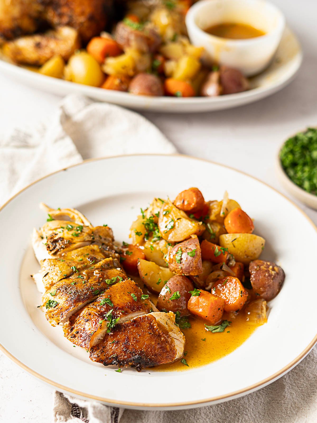 Sliced roasted bundt pan chicken breast served with roasted potatoes, carrots, and herbs, topped with sauce on a white plate.